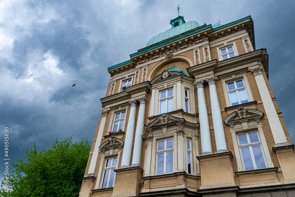Bogato zdobiona fasada kamienicy w Bielsku-Białej, kolumny, okna i pochmurne niebo.