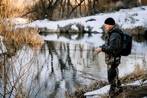 A fisherman with a fishing rod catches fish on the bank of a snow-covered river in early spring