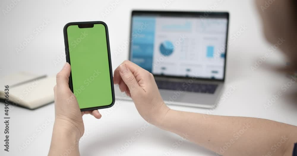 Chroma Key Mock-Up on Smartphone in Hand.Woman Using Phone with Green Screen. Laptop With Charts On Screen And Notepad In Background Chroma Key Mock-Up on Smartphone in Hand.Woman Using Phone with Green Screen. Laptop With Charts On Screen And Notepad In Background