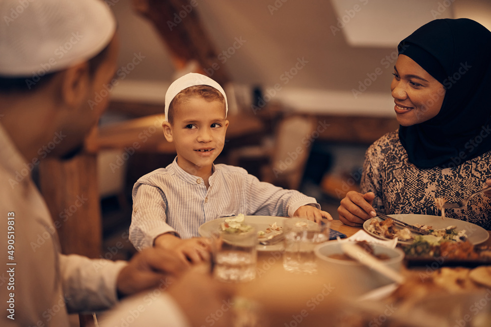 Fototapeta premium Happy Muslim boy talks to his parents during Ramadan meal at dining table.
