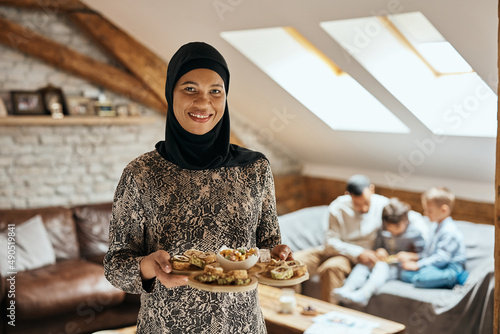 Happy black Muslim woman holds tray with dessert and looking at camera. photo