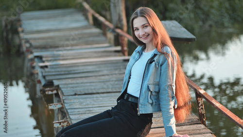 A young girl with long hair poses by the bridge on the river.