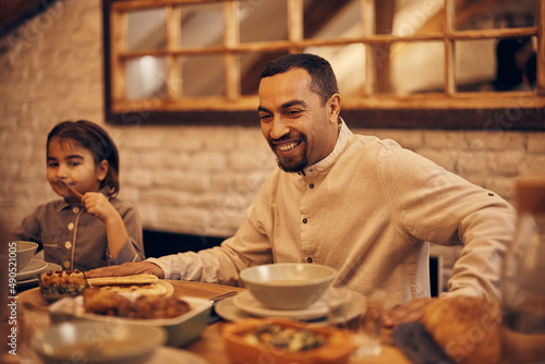 Happy Muslim father eats dinner with his family on Ramadan at home.