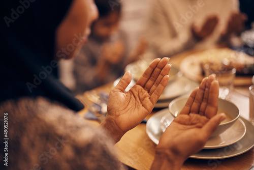 Close-up of black Muslim woman prays with her family at dining table.