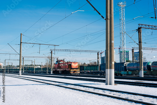 Overhead railway power lines and holding structures under blue sky and train