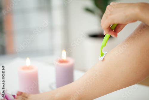 Young woman removing hair on legs with razor at bathroom