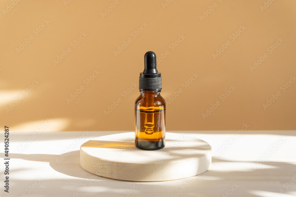 Mock-up of glass bottle, amber color, with a dropper lid, on beige background in rays of sunlight. Face serum close-up. Concept of beauty industry, body care Mock-up of glass bottle, amber color, with a dropper lid, on beige background in rays of sunlight. Face serum close-up. Concept of beauty industry, body care