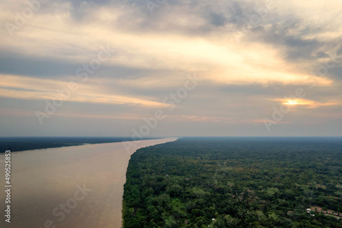 Aerial panorama view of the Amazon River and forest at sunset, with a small village, during the wet season