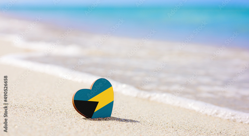 Obraz premium Flag of the Bahamas in the shape of a heart on a sandy beach. The concept of the best vacation in Bahamas
