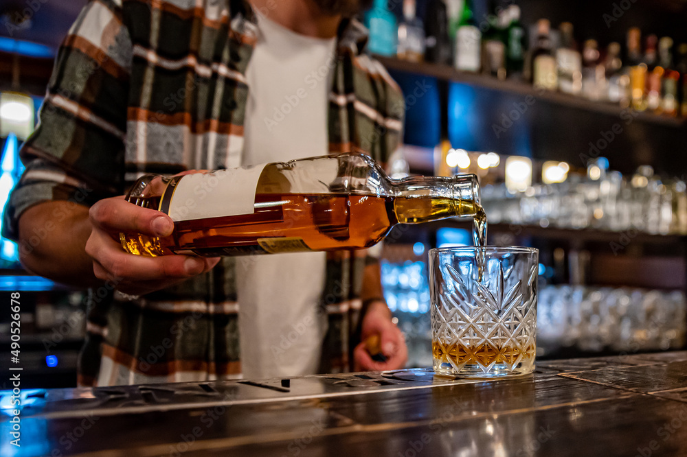 Barman pouring whiskey from bottle on glass in bar