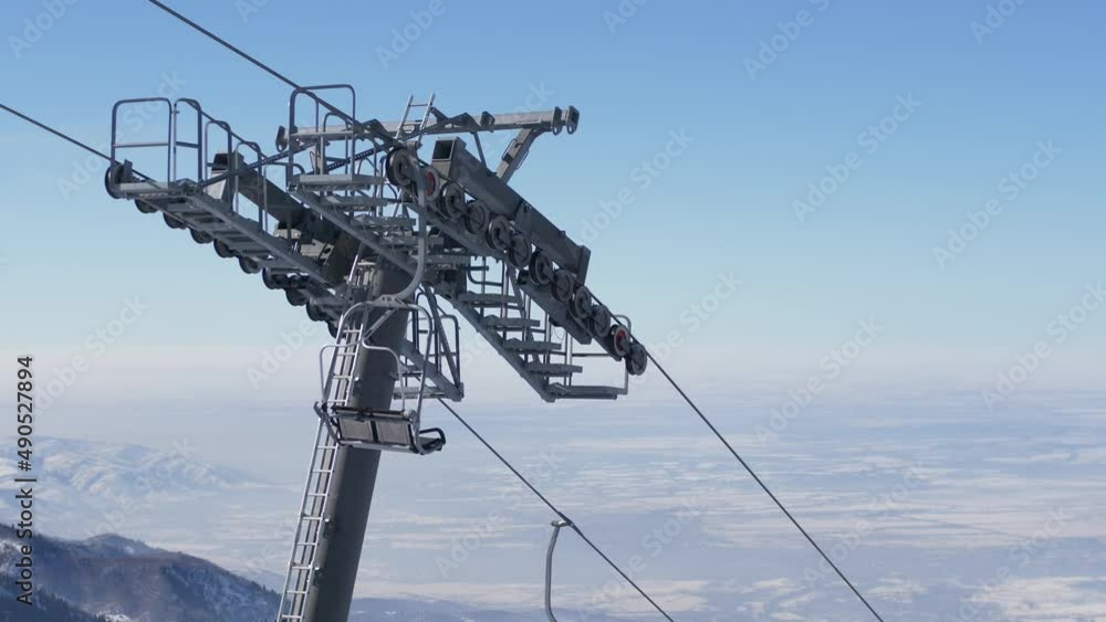 An empty chair lift moves in the snowy mountains on a bright sunny winter day high in the mountains against the backdrop of the valley below. An empty chair lift moves in the snowy mountains on a bright sunny winter day high in the mountains against the backdrop of the valley below.