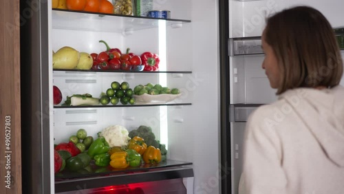 Woman taking raw food from refrigerator. Refrigerator full of healthy food. fruits and vegetables