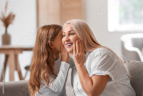 Little girl telling secret to her grandma at home