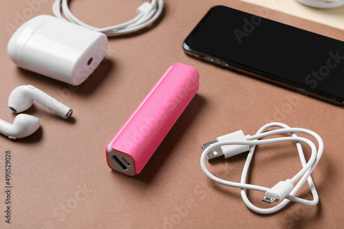 Power bank with USB cable, earphones and smartphone on brown background, closeup