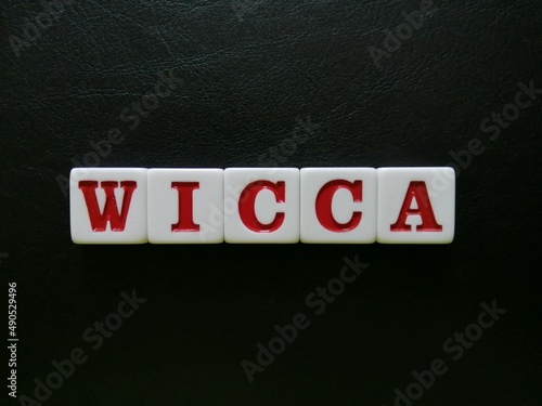 Photo The word WICCA is spelled with white and red tiles on a black leather background