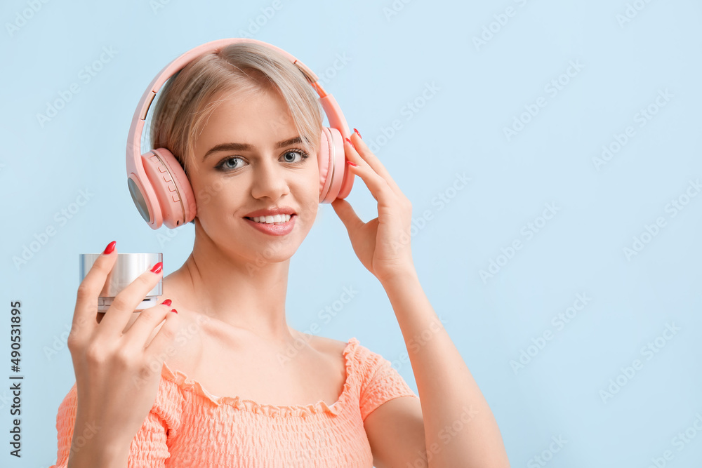 Young woman with modern headphones holding wireless portable speaker on blue background Young woman with modern headphones holding wireless portable speaker on blue background