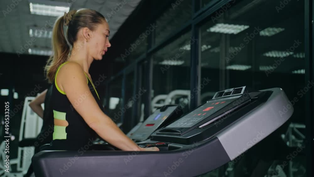 Fit Athletic Woman Running on the Treadmill, Doing Her Fitness Exercise. Muscular Women Activity Training in Modern Gym. Sports People Workout in Running track Fitness Center. Side View Slow Motion Fit Athletic Woman Running on the Treadmill, Doing Her Fitness Exercise. Muscular Women Activity Training in Modern Gym. Sports People Workout in Running track Fitness Center. Side View Slow Motion