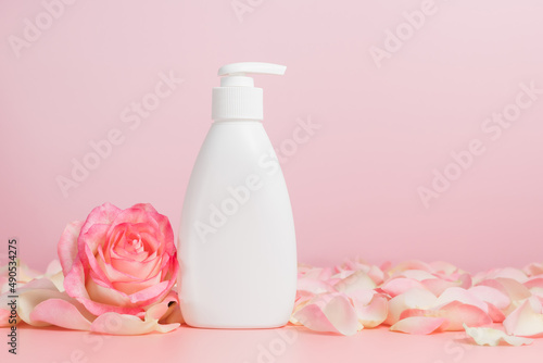 White mockup cosmetic liquid soap dispenser or body lotion bottle with pink lotion and petals