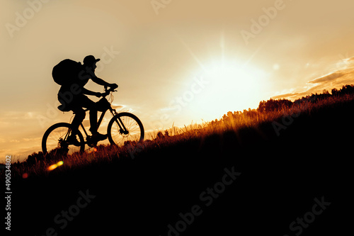 Obraz na plátně Silhouette of a man riding a bike uphill at sunset.