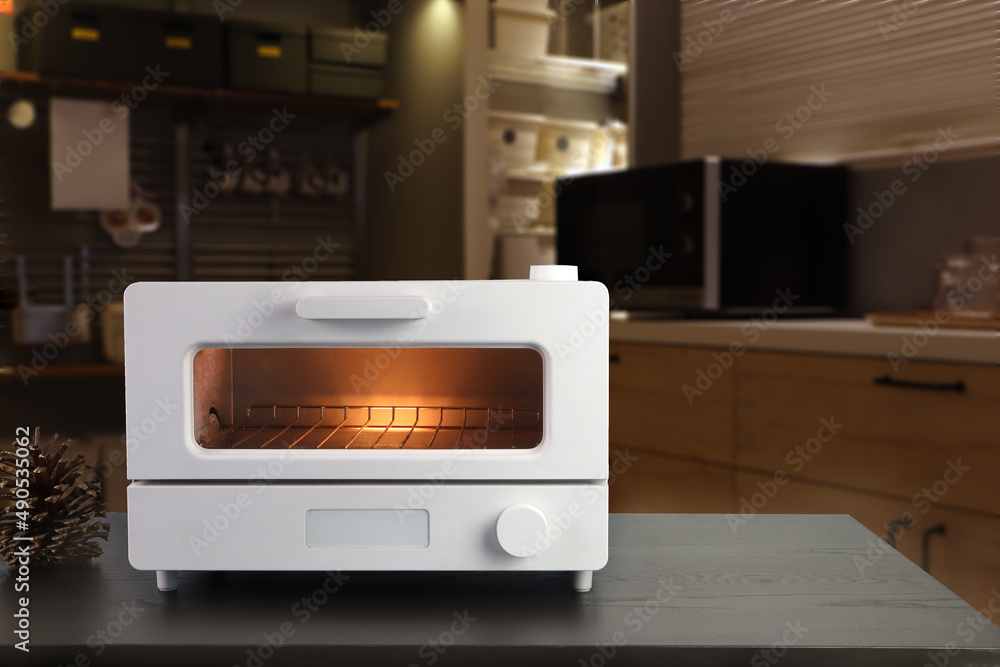 white modern design toaster oven is on the brown wooden table with background of nice dinner kitchen room during breakfast white modern design toaster oven is on the brown wooden table with background of nice dinner kitchen room during breakfast