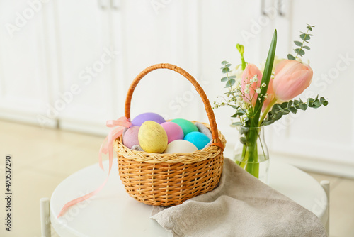 Gift basket with painted Easter eggs and flowers on table indoors