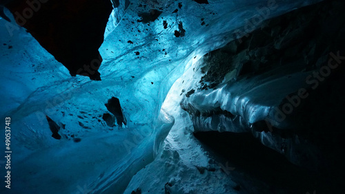 An ice cave of incredible beauty. The gradient of the blue ice shimmers. In places, the ice is clean and transparent. Huge stones frozen in ice are hanging. A mystical place. Bogdanovich Glacier.