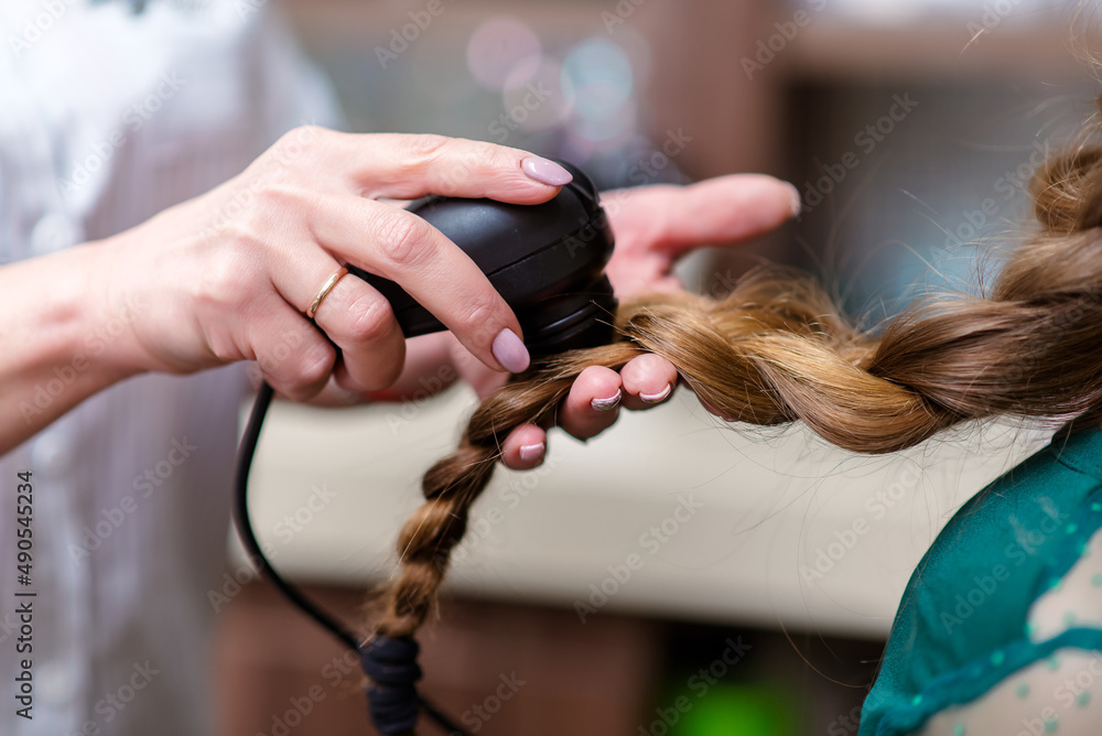 Naklejka premium Close-up of hairdresser examining client hair with a special apparatus for diagnostic hair and scalp in a hair shop.