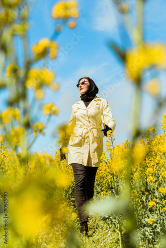 a stylish woman in a black scarf and sunglasses poses among a blooming yellow field of rapeseed under a bright spring sky. yellow and blue are the colors of the Ukrainian flag