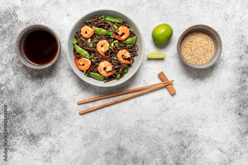 Stir fry buckwheat soba noodles with shrimps and vegetables in a bowl. Gray concrete grunge background. Asian traditional food. Top view. Stir fry buckwheat soba noodles with shrimps and vegetables in a bowl. Gray concrete grunge background. Asian traditional food. Top view.