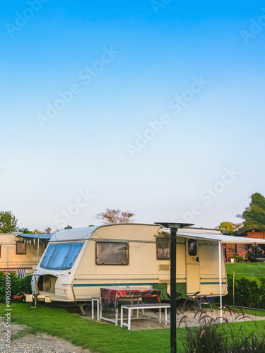 Cozy retro travel trailer Caravan on green grass before sunset near riverside in peaceful countryside. Family vacation travel RV, holiday trip in motorhome. Outdoor and Recreational Vehicles Theme. © JinnaritT