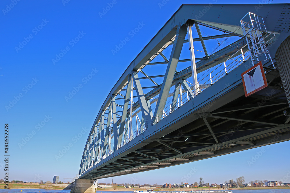 Nijmegen, Netherlands - February 27. 2022: View on truss railway bridge over river waal against blue sky