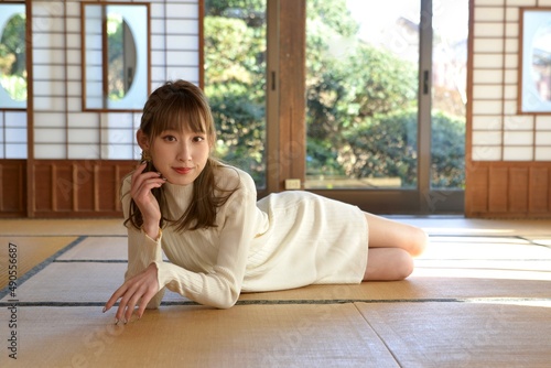 畳の上に横たわり頬杖をつく白いワンピースを着た若い女性 © Shoji