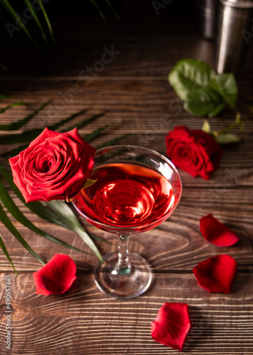 Delicious refreshing beverage drink red cocktail with red rose and petals on wooden table. Romantic, Valentines day concept.