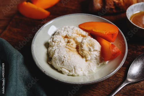 Homemade ricotta cheese or cheese curd served with fresh persimmon and honey and croissante on wooden background. Healthy breakfast. Haze effect. Selective focus