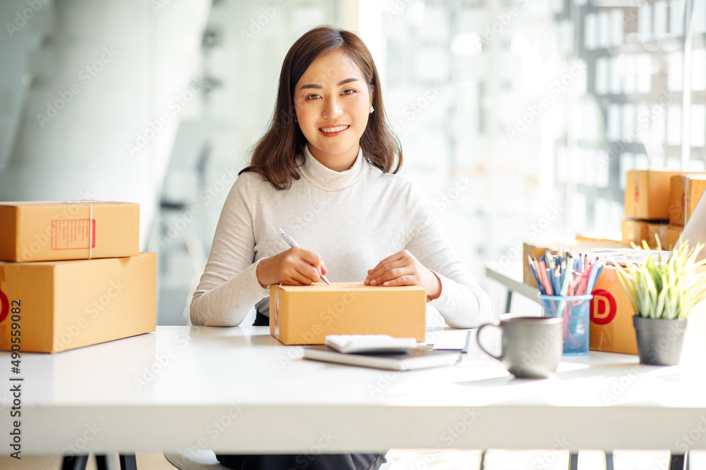 Startup SME small business entrepreneur SME or freelance Asian woman using a laptop with box, Young success Asian woman with her hand lift up, online marketing packaging box and delivery, SME concept. Startup SME small business entrepreneur SME or freelance Asian woman using a laptop with box, Young success Asian woman with her hand lift up, online marketing packaging box and delivery, SME concept.