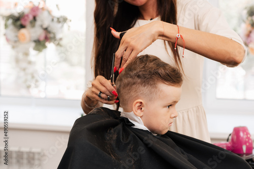 Shooting in a beauty salon. A barber cuts a little boy's hair with scissors