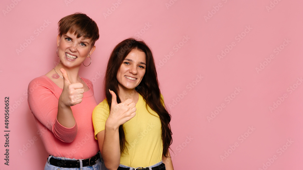 A studio shot of two young girl friends on a bright background shows an approving hand sign. A place for your text. A studio shot of two young girl friends on a bright background shows an approving hand sign. A place for your text.
