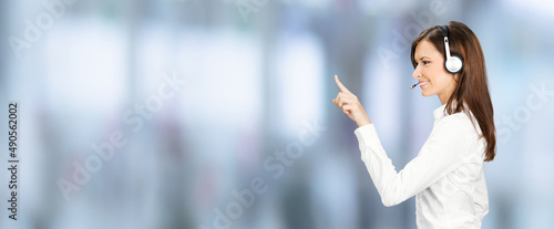 Call center service. Profile side image of customer support phone sales operator in headset showing pointing finger clicking at copy space, imaginary or text, standing over blurred office background.