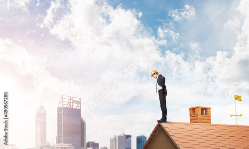 Businessman looking down from roof and modern cityscape at background. Mixed media