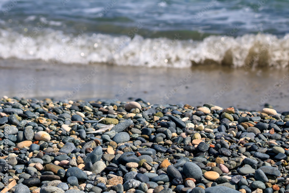 Various stones and pebbles in front of blurry foamy sea wave at the beach in sunlight Various stones and pebbles in front of blurry foamy sea wave at the beach in sunlight