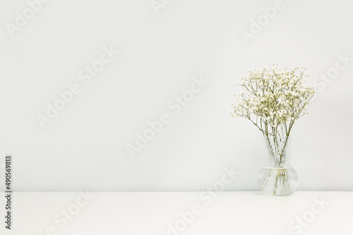 Bouquet of white pastel flowers gypsophila in a vase on table against the background of a white wall. Minimalistic scandinavian background mockup with copy space.