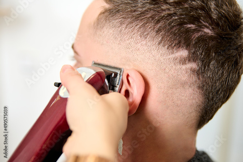 a man sitting in the barbershop while the hairdresser was styling his hair with an electric clipper