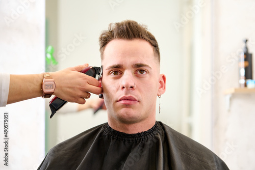a man sitting in the barbershop while the hairdresser was styling his hair with an electric clipper
