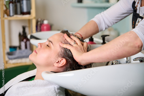 Hairdresser washes the head of a brunette girl with shampoo in the beauty salon