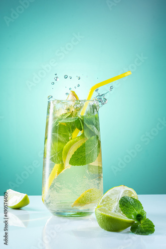 Thirst-quenching drink with mint and lemon. Glass with water, mint and lemon. Spray over glass. Bright turquoise background.