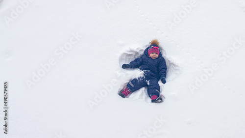 A baby girl lies in the snow in winter and waves her hands portraying an angel