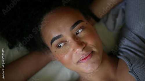 A smiling happy black person lying down in bed feeling happy