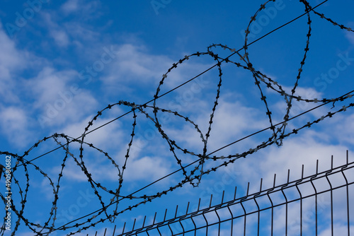 Barbed wire fence on background with blue sky and white clouds. Concept of freedom and prison escaping, migration metaphor