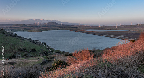 View of Bental water reservoir, the Golan hills with wind turbines and the Hermon Mounrain Range at sunset as seen from Mount Bental summit, Golan Heights, Israel.