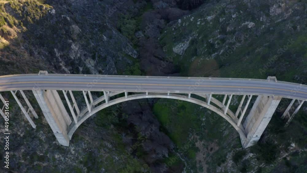 Aerial view cars passing Bixby Creek Bridge PCH Highway 1 in California. Aerial view of the picturesque arch bridge standing over the canyon. Cars move across the bridge. Aerial view cars passing Bixby Creek Bridge PCH Highway 1 in California. Aerial view of the picturesque arch bridge standing over the canyon. Cars move across the bridge.